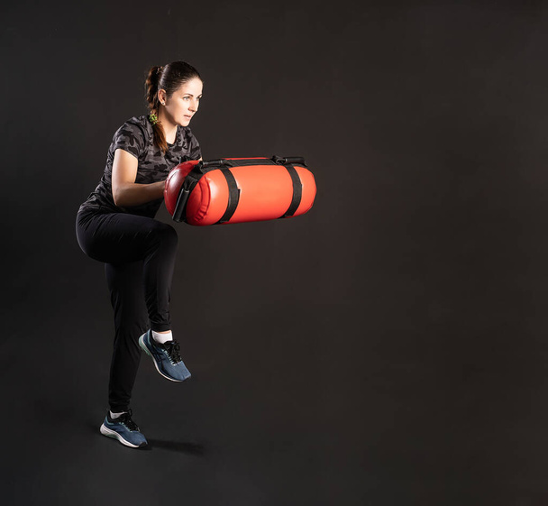 Fitness woman with Aqua Bag, stretches her leg. Engaged in sports on a black background Smiling with gentle lips - 写真・画像