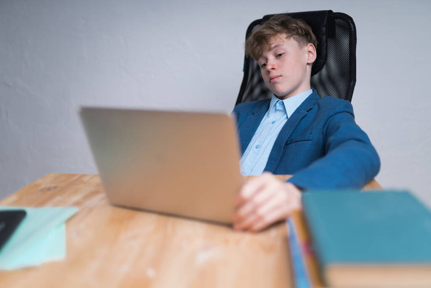 A mid shot of a serious Caucasian teenage boy in school uniform during his online classes. Online education concept - Foto, imagen