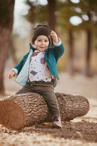 a boy in a green warm jacket and a knitted hat is sitting on a tree. He's happy. Image with selective focus - Foto, Bild
