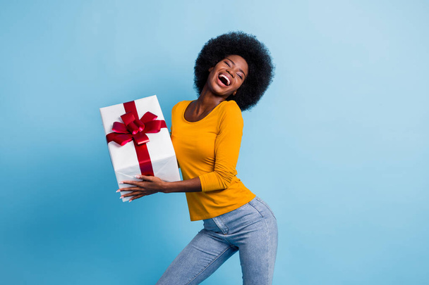 Photo portrait of happy smiling black skinned woman keeping wrapped gift laughing dancing isolated on bright blue color background - Foto, imagen
