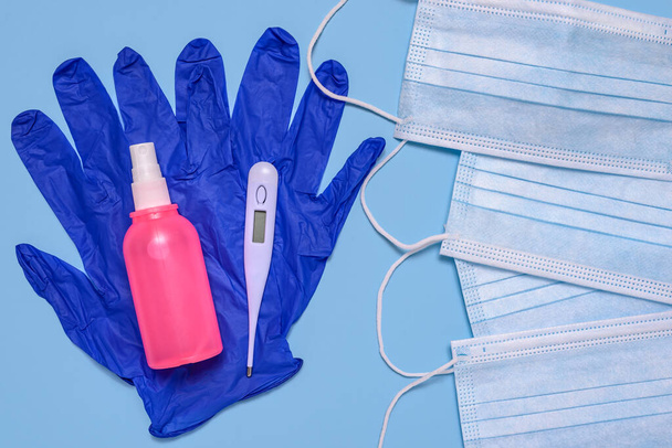 Medizinische chirurgische Gesichtsmasken, Schutzhandschuhe, antibakterielles antiseptisches Spray für Händedesinfektionsmittel und Thermometer zur Temperaturmessung des menschlichen Körpers auf hellblauem Hintergrund. - Foto, Bild