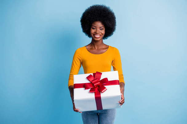 Photo portrait of happy smiling black skinned woman holding wrapped with red ribbon gift isolated on vibrant blue color background - Photo, image