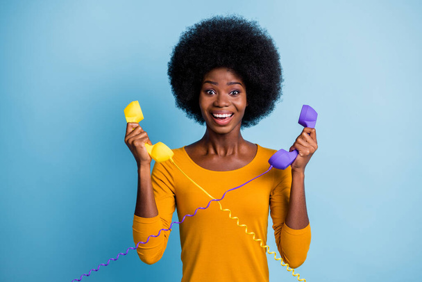 Photo portrait of black skinned woman holding two retro phone handsets with wires isolated on vivid blue color background - Foto, afbeelding
