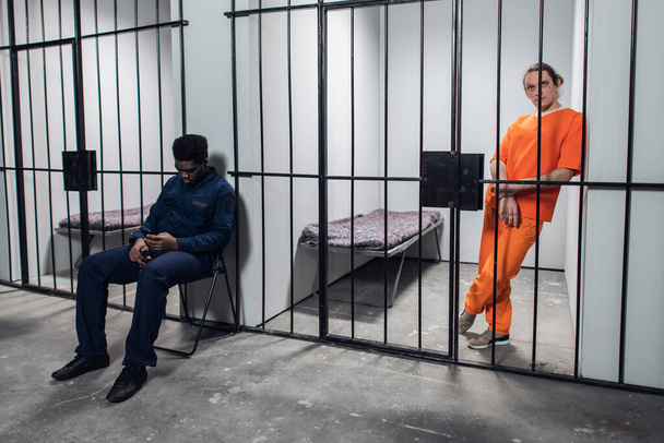 Ein Gefängniswärter bewacht Zellen mit zu lebenslanger Haft verurteilten Häftlingen in orangefarbenen Gefängnisuniformen. - Foto, Bild