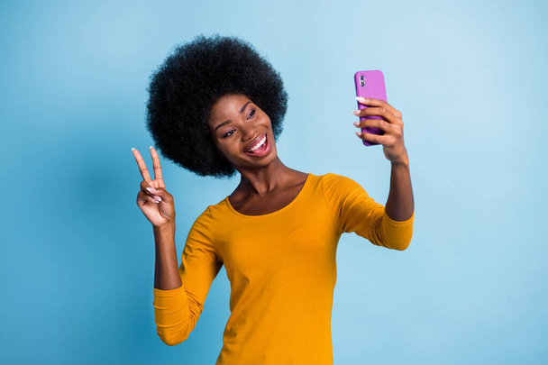 Photo portrait of pretty black skinned girl taking selfie smiling demonstrating v-sign isolated on bright blue color background - Fotó, kép