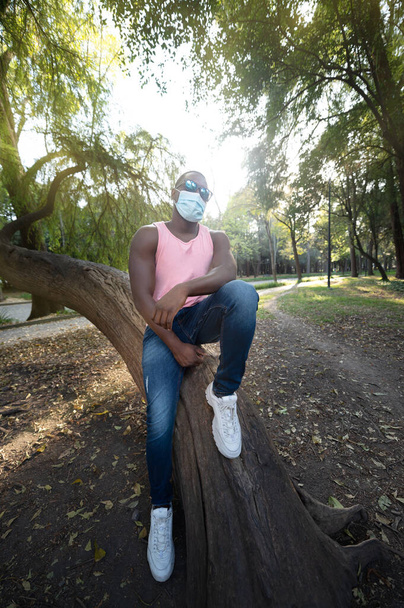 Ein junger schwarzer Mann mit Maske in der Covid-19-Pandemiesaison zum Schutz. Porträt eines jungen Afrikaners mit Gesichtsmaske im Park. - Foto, Bild
