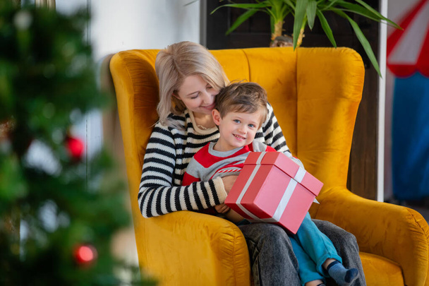 mam en zoon zitten in een fauteuil met een cadeau - Foto, afbeelding