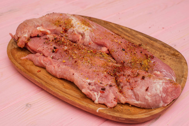 Ahşap bir tahtanın üzerinde pembe çiğ domuz bifteği var. İştah açıcı et. Ahşap tahtadaki domuz eti pembe arka planda - Fotoğraf, Görsel