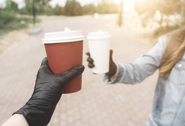 Girls in medical black latex gloves hold two paper coffee cups in their hands. The concept of protection from bacteria and viruses. Protect the coronavirus - Valokuva, kuva