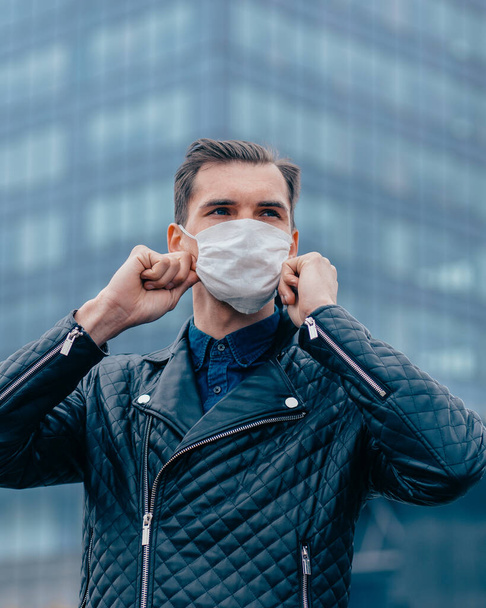 attractive man putting on a protective mask on a city street - Zdjęcie, obraz