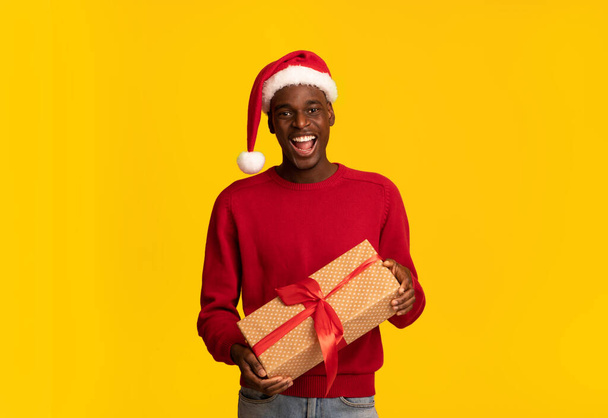 Enjoying Holidays. Cheerful Black Man In Santa Hat Holding Christmas Present Box - Zdjęcie, obraz