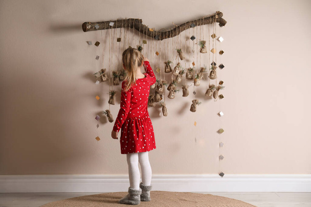 Маленькая девочка получает подарок от новогоднего календаря в помещении - Фото, изображение