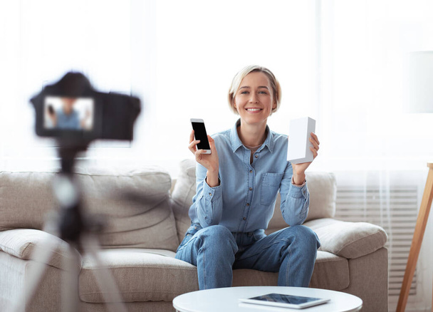 Pozitív női vlogger felvétel videó felülvizsgálata új okostelefon otthon - Fotó, kép