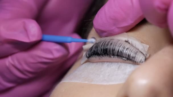 Face of young girl before eyelash lamination procedure in a professional beauty salon. The master washes off the black paint on the eyelashes during the eyelash curling procedure with a special brush - Footage, Video