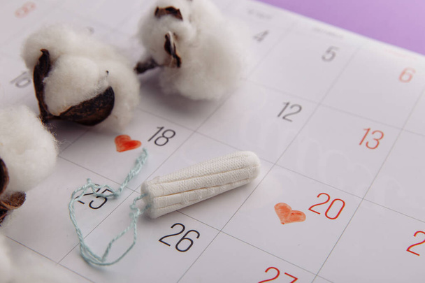 Menstruation Frau Hygienekonzept. Minimal flach liegend Menstruations-Tamppon und Kalender mit einem Baumwollzweig auf fliederfarbenem Hintergrund - Foto, Bild