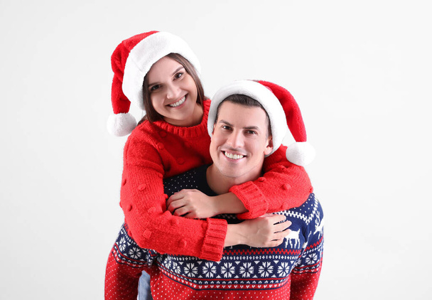 Hermosa pareja feliz en sombreros de Santa y suéteres de Navidad sobre fondo claro - Foto, Imagen