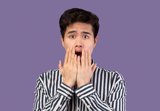 Scared asian man grimacing, shocked at purple studio - Photo, Image