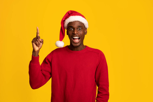 サンタ・ハットで興奮した黒人男性が指を指差す、クリスマスのアイデアを持つ - 写真・画像