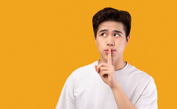 Asiatischer Mann legt Finger auf seine Lippen und macht Schweigezeichen - Foto, Bild