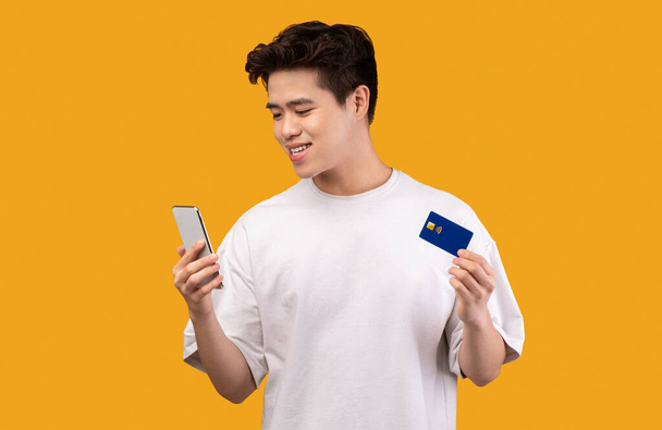 asiático chico holding crédito tarjeta y celular en estudio - Foto, imagen