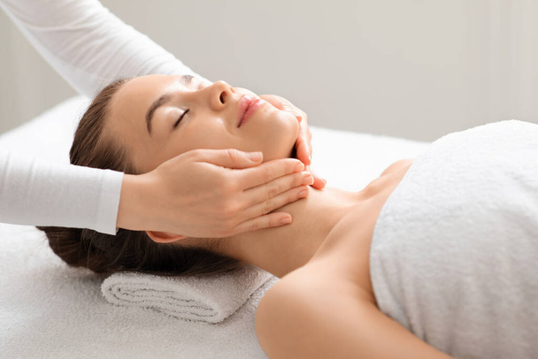 Joyful jovem mulher relaxante durante a massagem lifting rosto - Foto, Imagem