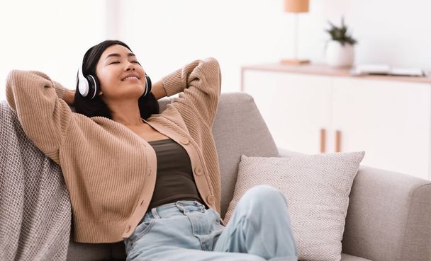 Calma mujer asiática escuchando música usando auriculares - Foto, imagen