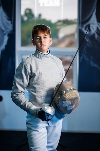 Child in a fencing suit with a sword in hand in the studio. Young boys practice and practice fencing. Sports, healthy lifestyle. - Фото, зображення