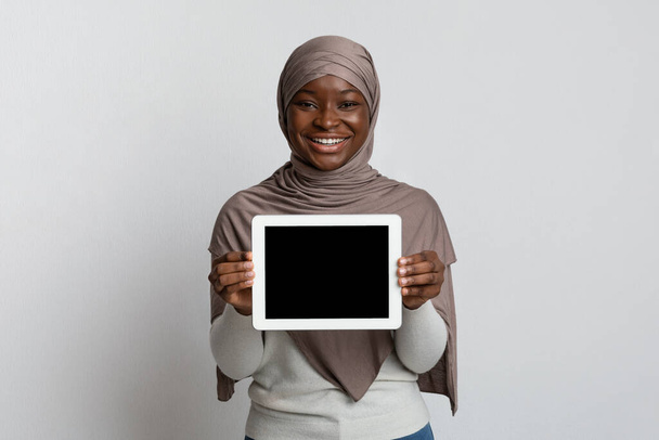 Burla de sonriente mujer musulmana africana sosteniendo tableta digital con pantalla negra - Foto, imagen