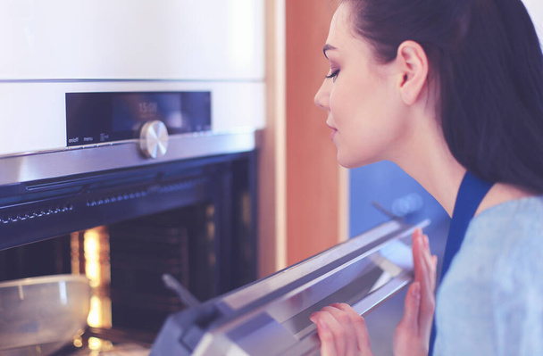 Beautiful young woman checking how her cake is doing in the oven - Foto, Bild