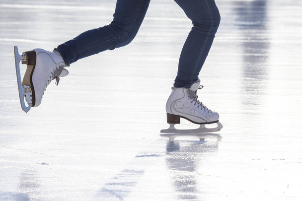 piernas de una mujer en pantalones vaqueros azules y patines blancos en una pista de hielo. pasatiempos y ocio. deporte de invierno - Foto, Imagen