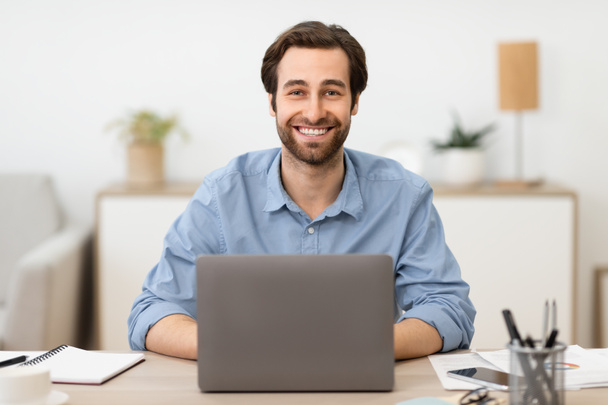 Pomyślny biznesmen siedzi na laptopie w miejscu pracy w nowoczesnym biurze - Zdjęcie, obraz