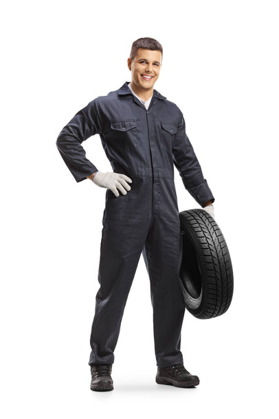 Full length portrait of an auto mechanic worker holding a car tire and smiling isolated on white background - Zdjęcie, obraz