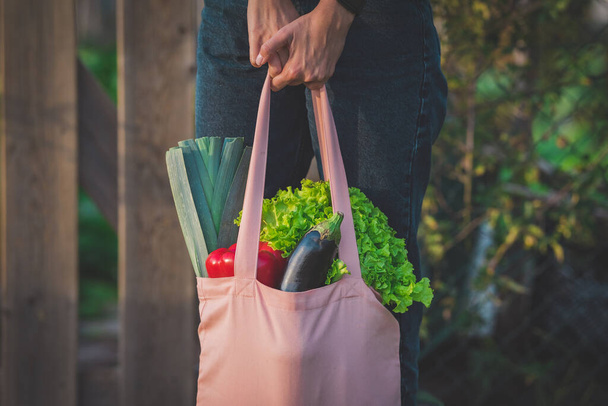 ピンクの再利用可能な食料品袋新鮮なバイオ野菜でいっぱいの女性の手。廃棄物ゼロ、プラスチックフリーコンセプト - 写真・画像