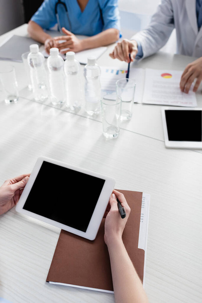 Cropped view of nurse holding digital tablet with blank screen near paper folder and colleagues on blurred background  - Foto, Imagen