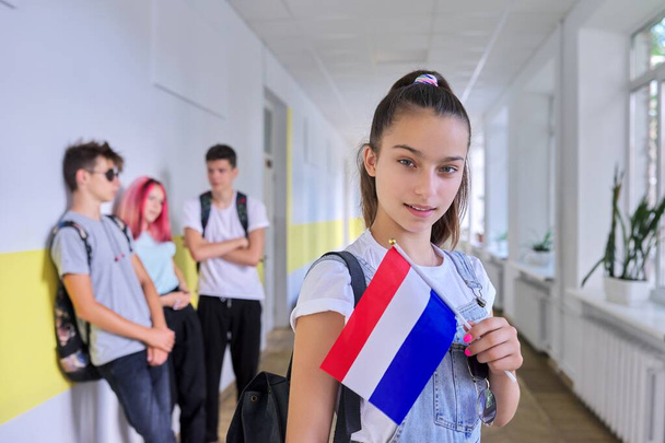 Student teenager girl with Netherlands flag inside school, school children group background - Photo, image