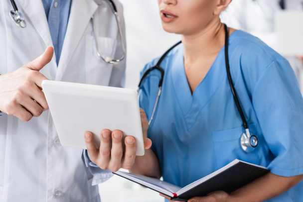 Cropped view of doctor holding digital tablet near nurse with notebook in clinic  - Foto, immagini