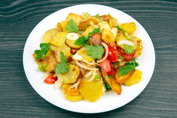 batatas fritas cozidas com ervas e legumes em uma placa branca em uma mesa de madeira - Foto, Imagem