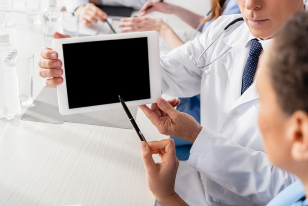Siyahi hemşireler dijital tableti işaret ediyor. Doktorun yanında boş ekran ve bulanık arkaplan üzerinde meslektaşları var.  - Fotoğraf, Görsel
