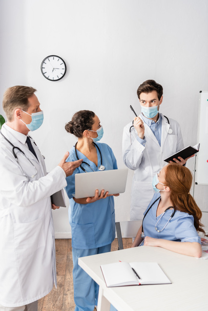 Doctor with idea gesture standing near multiethnic colleagues near workplace - Photo, Image