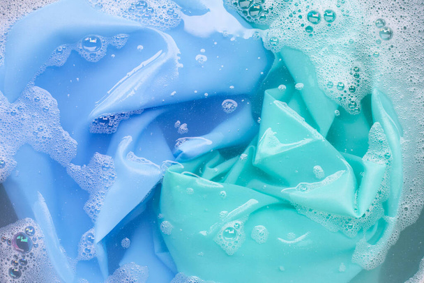 Vestiti di colore immersi nella dissoluzione dell'acqua detergente in polvere. Concetto lavanderia - Foto, immagini