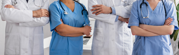 Vista recortada de enfermeras multiculturales y médicos con brazos cruzados de pie juntos en el hospital, pancarta - Foto, Imagen