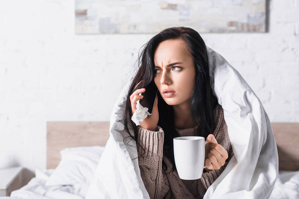 malato giovane bruna donna con bevanda calda e tessuto talkign su smartphone a letto - Foto, immagini