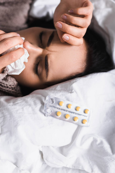 sick young brunette woman with pills and runny nose in bed - Foto, Bild