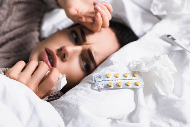 enferma joven morena mujer con píldoras y tejido en la cama - Foto, Imagen