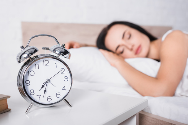 classic alarm clock and blurred young brunette woman sleeping in bed on background - Fotografie, Obrázek