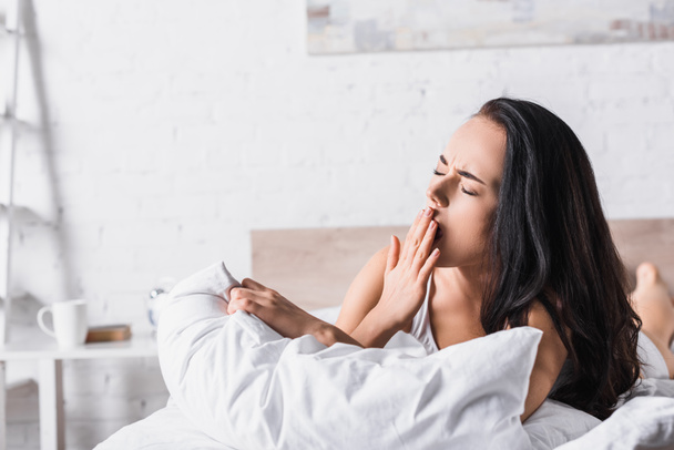 mladá brunetka žena zívání v posteli - Fotografie, Obrázek