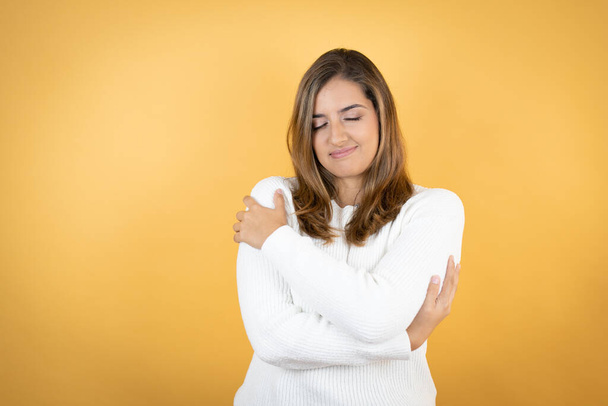 Young caucasian woman over isolated yellow background hugging oneself happy and positive, smiling confident - Фото, изображение