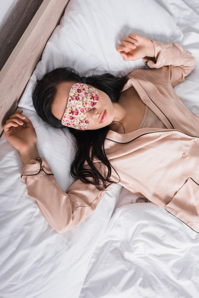 top view of young brunette woman sleeping in bed in sleep mask - Fotó, kép