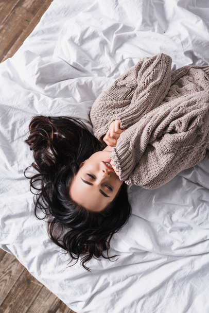 top view of young brunette woman in sweater sleeping in bed at morning - Photo, Image