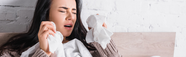 mujer morena joven enferma en suéter estornudando en la cama con pañuelos, pancarta - Foto, Imagen